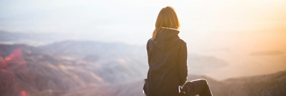 person sitting on top of gray rock overlooking mountain during daytime